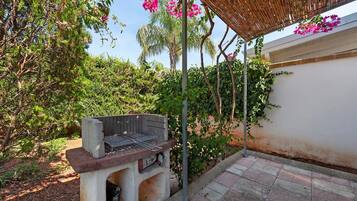 Una parrilla para barbacoa montada al aire libre, con una pérgola arriba.