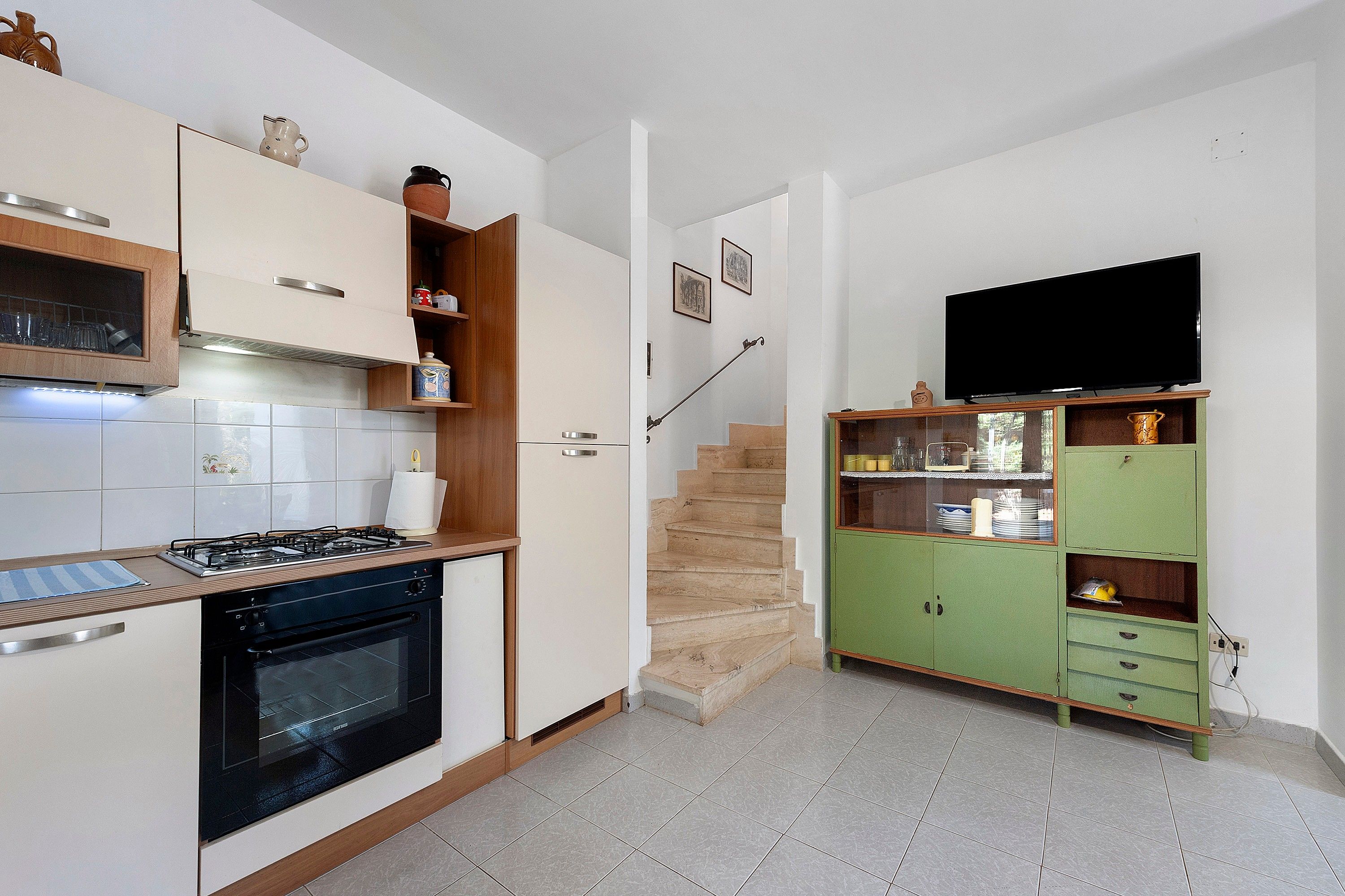 A compact kitchen with a gas stove, oven, and a dining area with a green cabinet and a television.