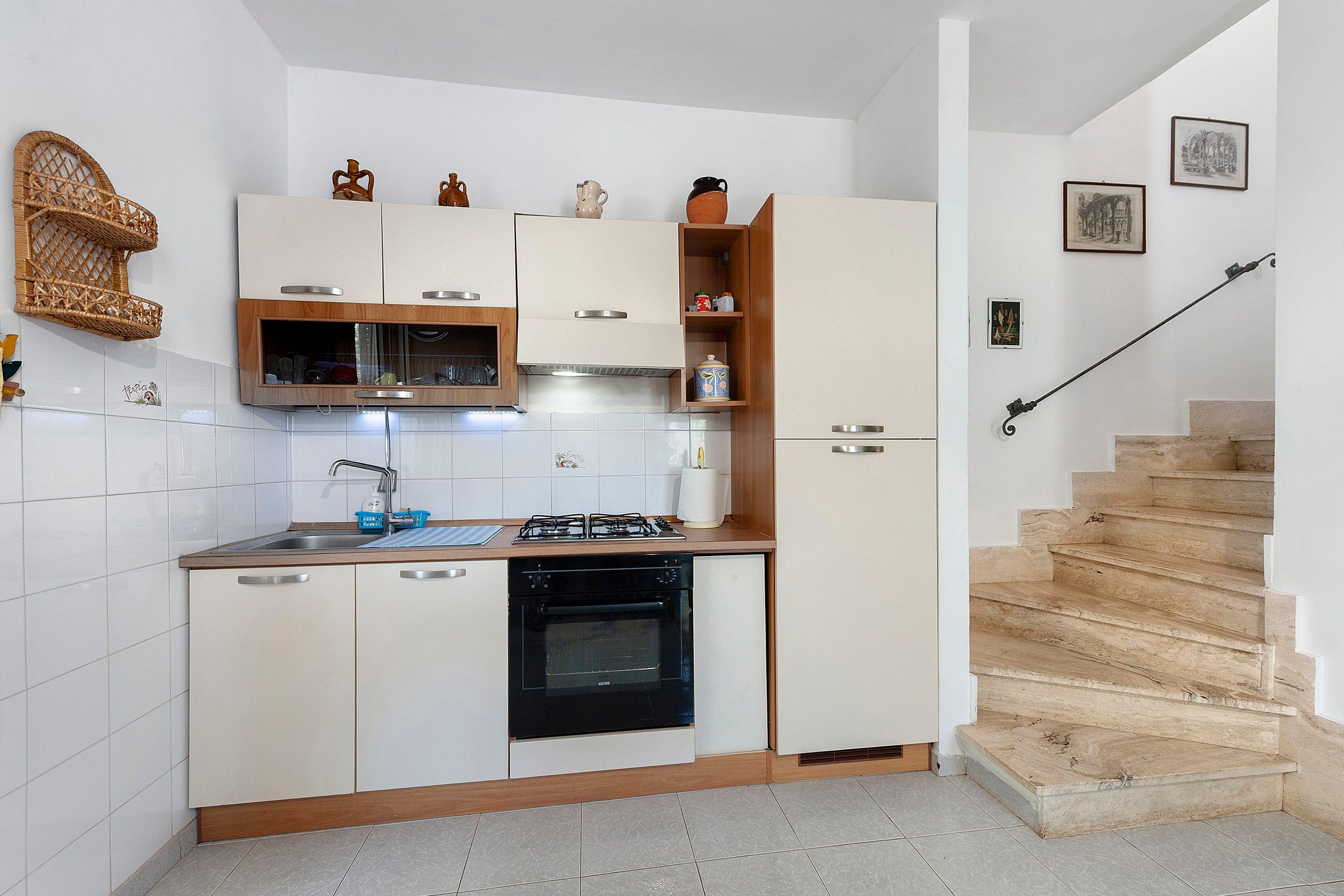 Una cocina compacta con armarios blancos, horno integrado y un lavamanos.