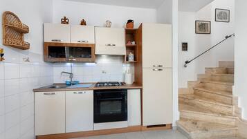 Una cocina compacta con armarios blancos, horno integrado y un lavamanos.