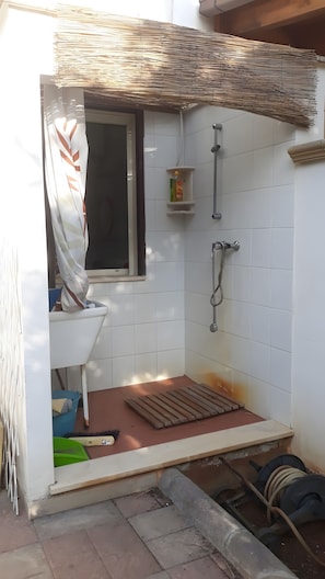Ein kleines Badezimmer mit Fliesen, einer Dusche, einem Fenster und einem Ablagefach mit Toilettenartikeln.