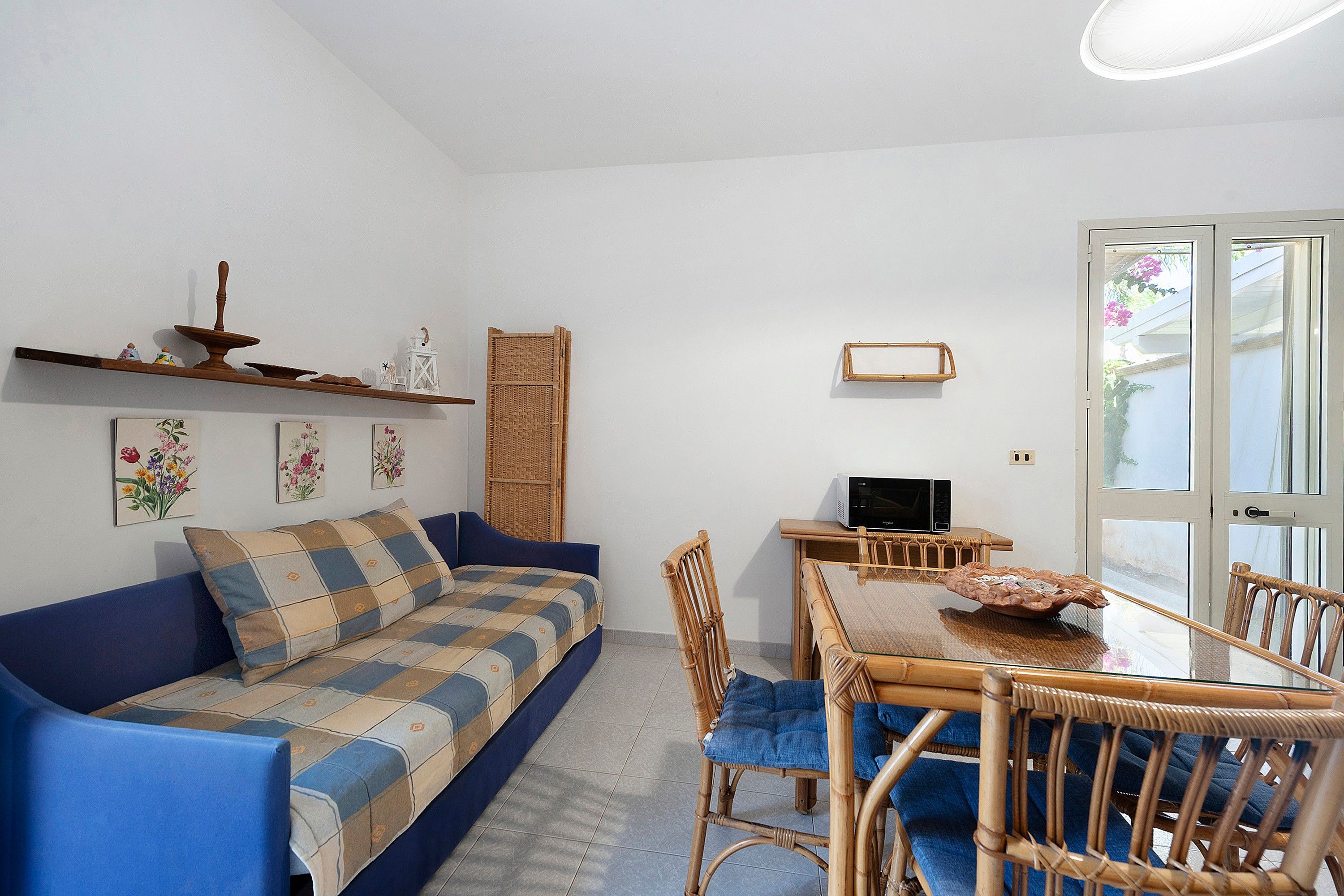 Un salon comprenant un canapé, une table à manger avec des chaises, un téléviseur et une porte donnant sur une vue agréable.