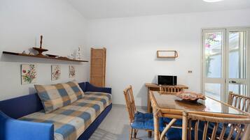 Un salon comprenant un canapé, une table à manger avec des chaises, un téléviseur et une porte donnant sur une vue agréable.