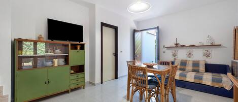 A living room with a dining table, chairs, a television, and a sofa.