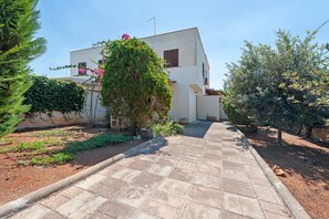 A paved pathway leading to a building with a white facade and a small garden area with various plants and shrubs.