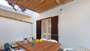 A wooden table with white chairs, a window with shutters, and a bamboo roof. - Apartment 'Villetta Sea Sun' with Shared Pool, Private Terrace, and Air Conditioning (Eurovillage)