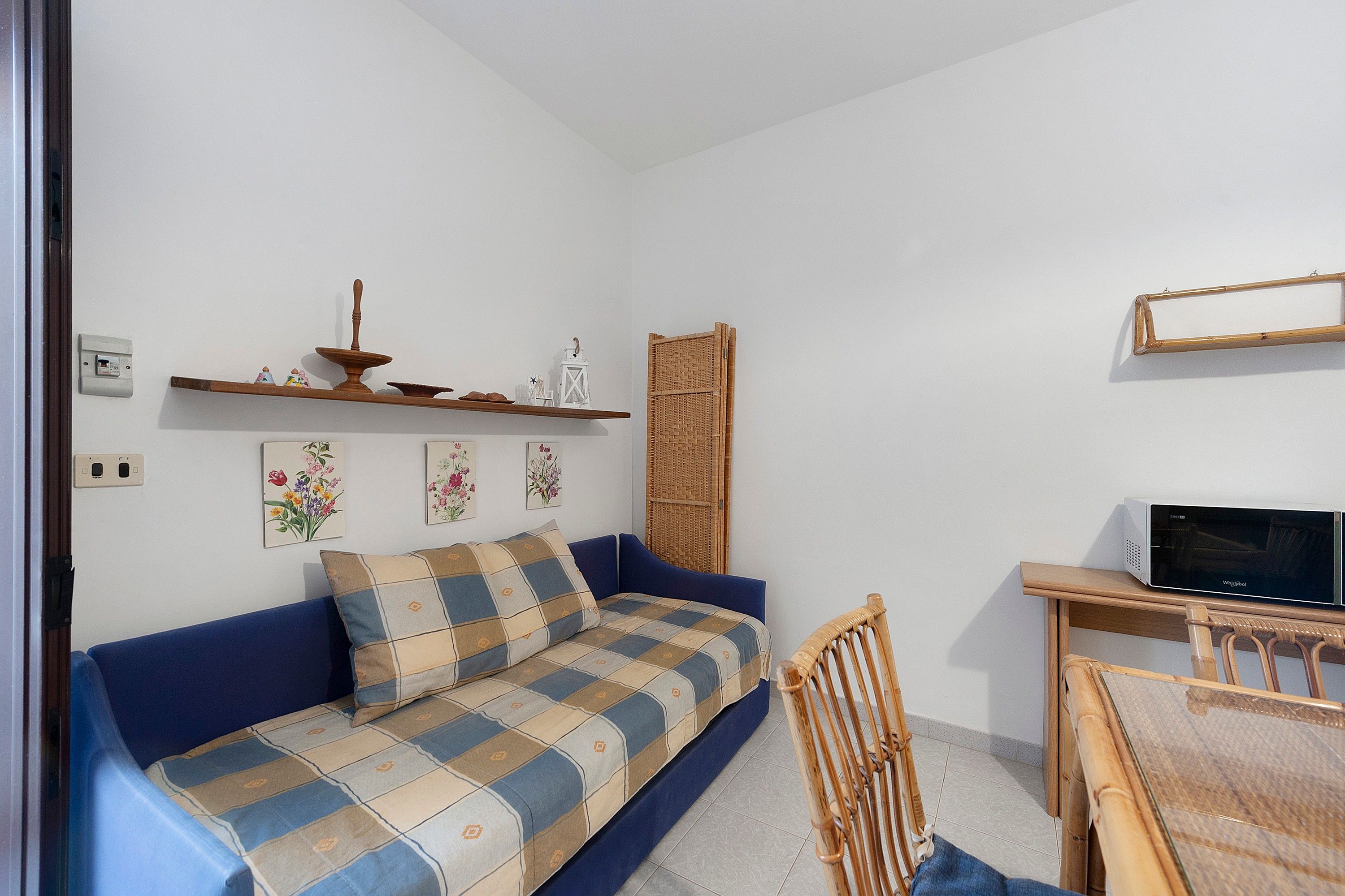 A small, cozy room with a blue sofa, a wooden chair, a dining table, and a television.