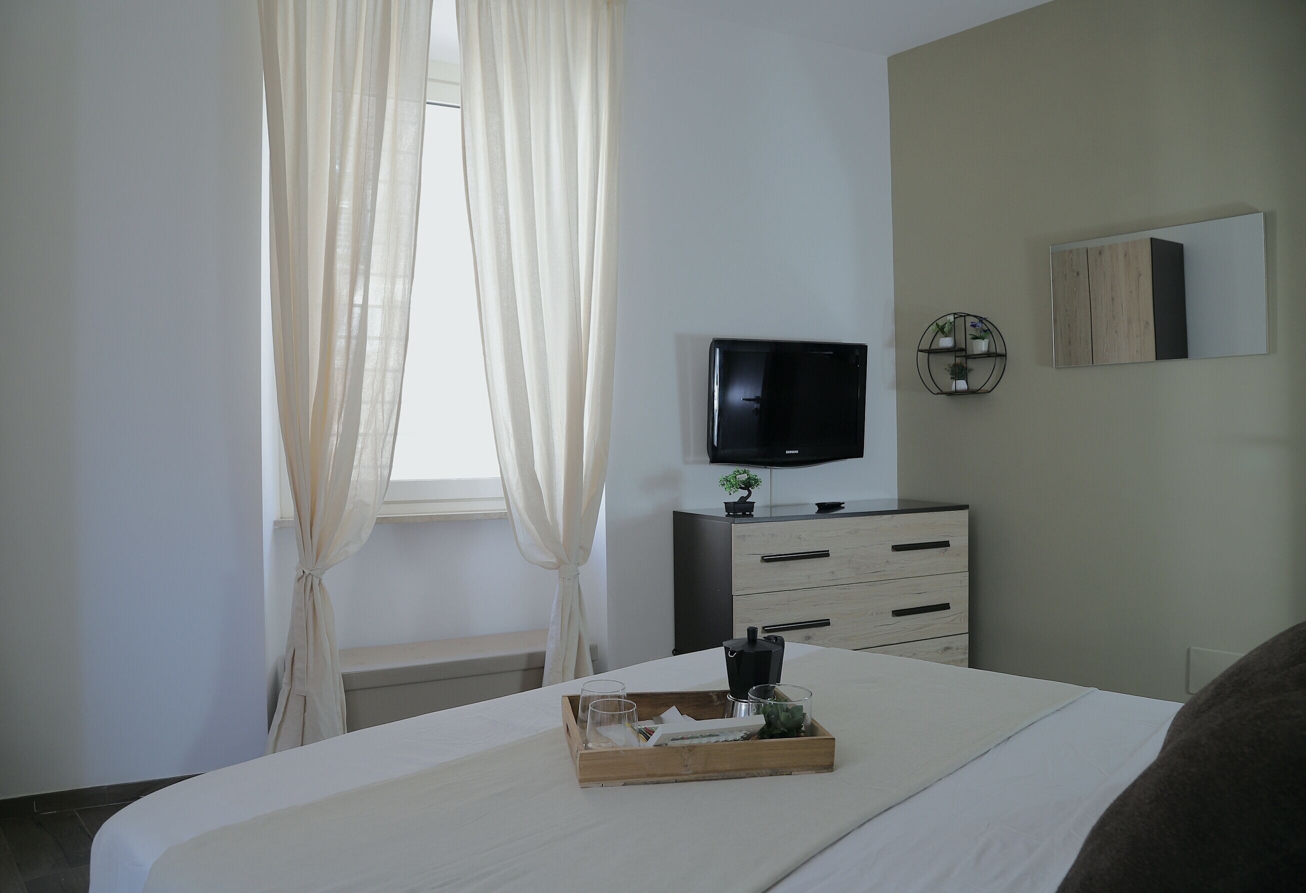 Ein Hotelzimmer mit Bett, Fernseher, Kommode, Spiegel und einem Fenster mit Vorhängen.