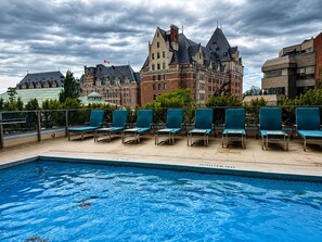 Una piscina con lettini, un ampio edificio storico sullo sfondo e un cielo nuvoloso.