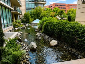 Un cortile tranquillo con una piccola fontana, circondato da piante rigogliose e edifici moderni.