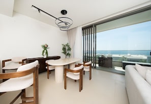Un salon moderne avec un coin repas, de grandes fenêtres et une vue sur l’océan.
