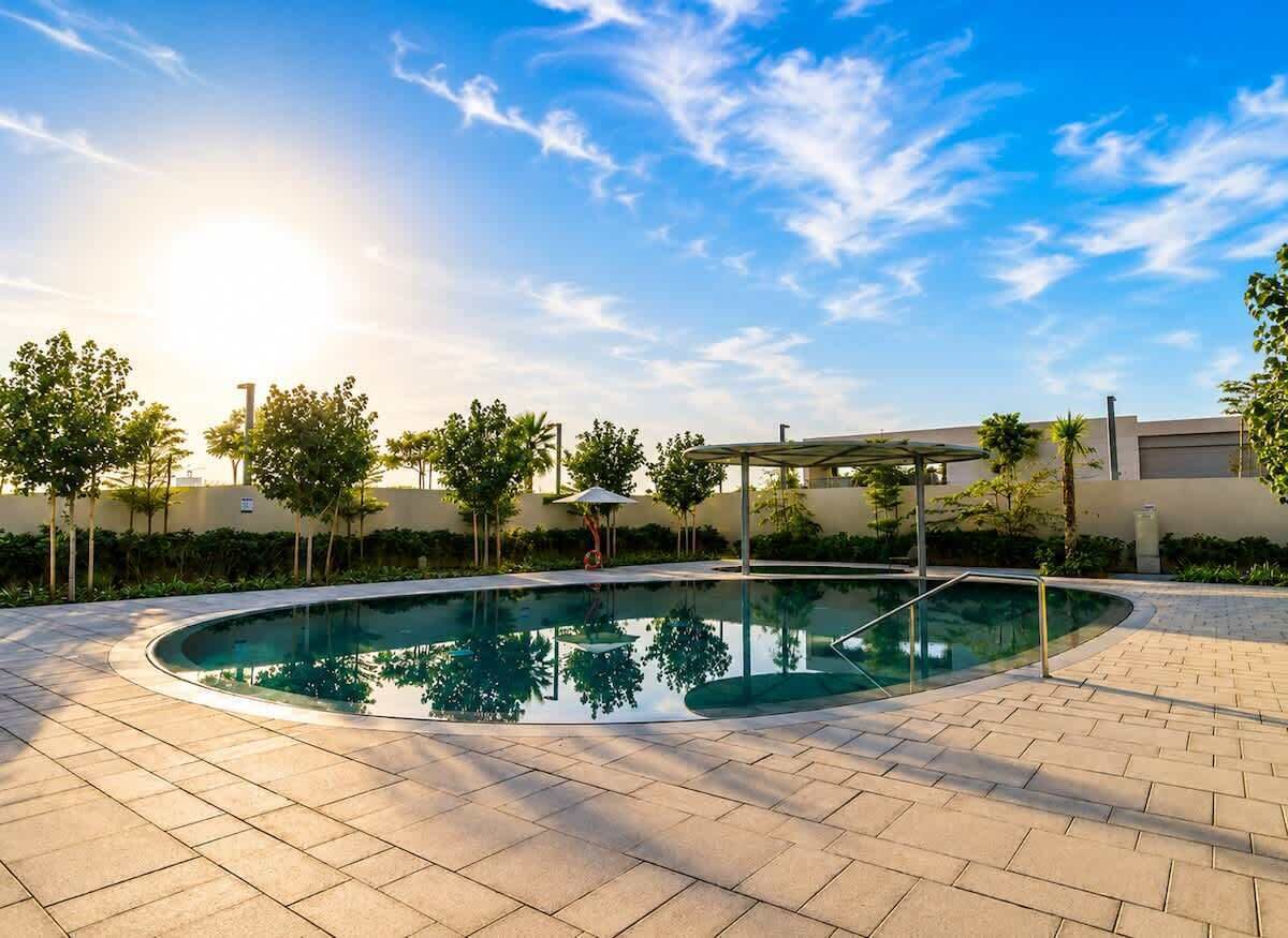 Una piscina con bordo piastrellato, circondata da alberi e un edificio sullo sfondo.