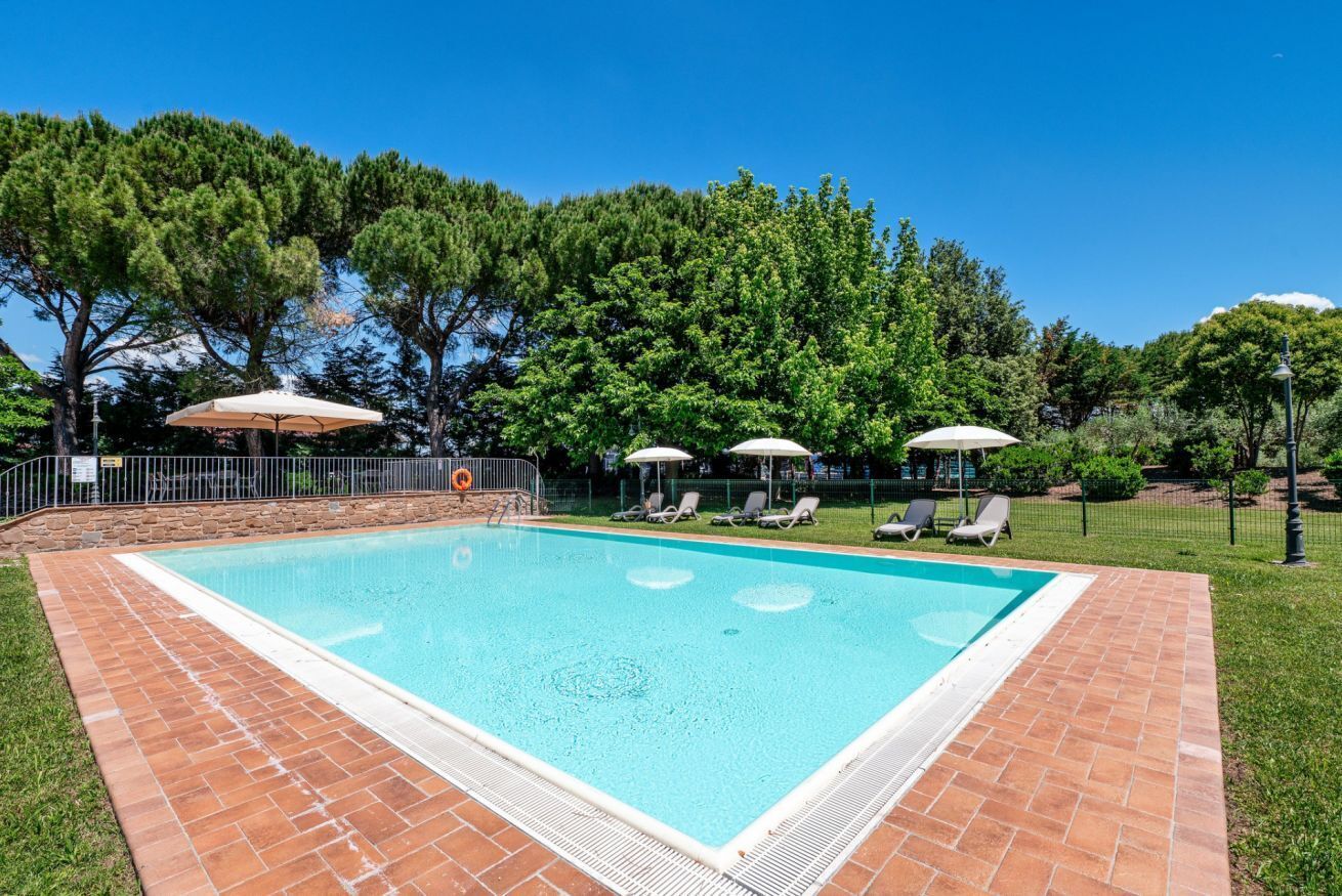 A rectangular swimming pool with a tiled border, surrounded by a grassy area and trees.