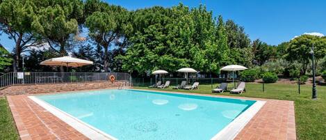 Une piscine rectangulaire bordée de carreaux, entourée d’une pelouse et d’arbres.