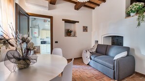 A living room with a sofa, a dining table with chairs, a fireplace, and a kitchen area in the background. - GuestHost - Il Casale dei Gelsi - Narciso (San Martino In Campo)