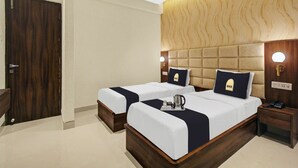A hotel room with two beds, a wooden headboard, a ceiling fan, and a nightstand with a phone. - Townhouse Oak Hotel Lake View Royal (Kolkata)
