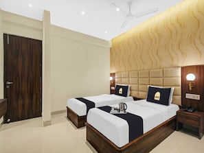 A hotel room with two beds, a wooden headboard, a ceiling fan, and a nightstand with a phone. - Townhouse Oak Hotel Lake View Royal (Kolkata)