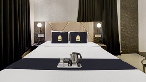 A hotel room with a large bed, two pillows with 'OAK' branding, bedside lamps, a tray with a kettle, and a telephone. - Townhouse Oak Hotel Lake View Royal (Kolkata)