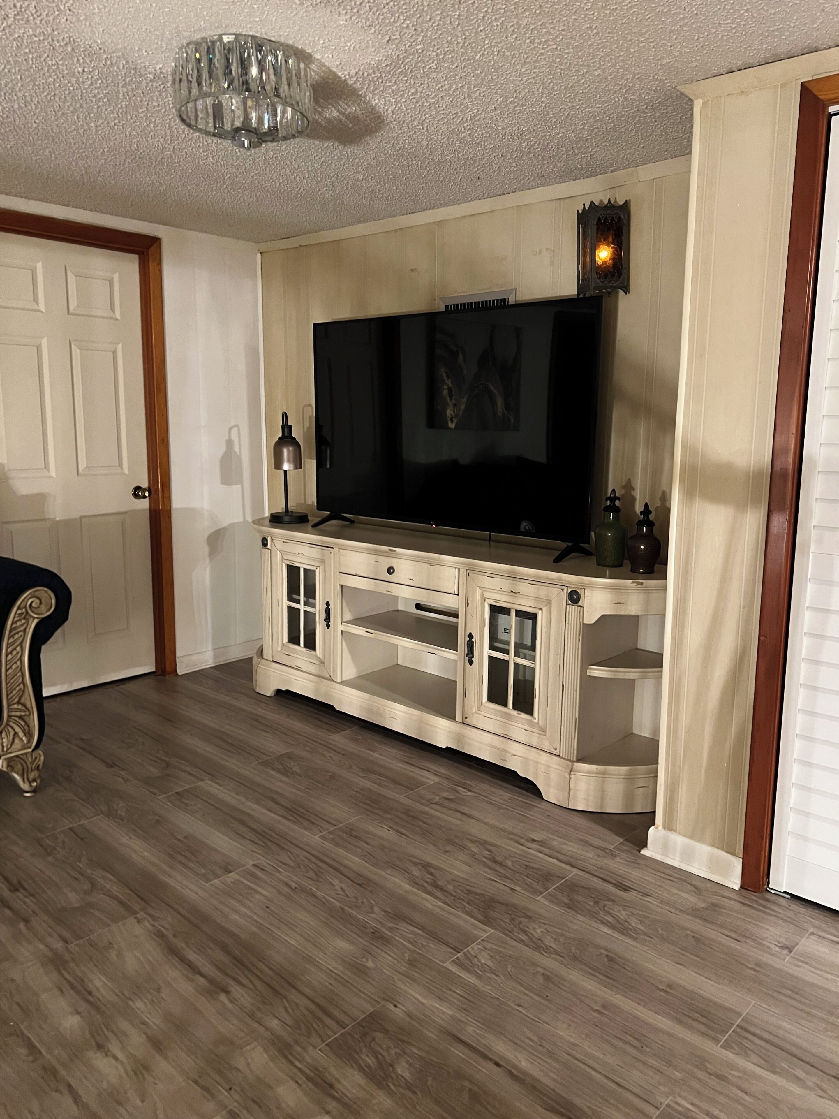 Ein Wohnzimmer mit einem großen Flachbildfernseher auf einer Holzkommode, einer Kandelaber und einer Tür.