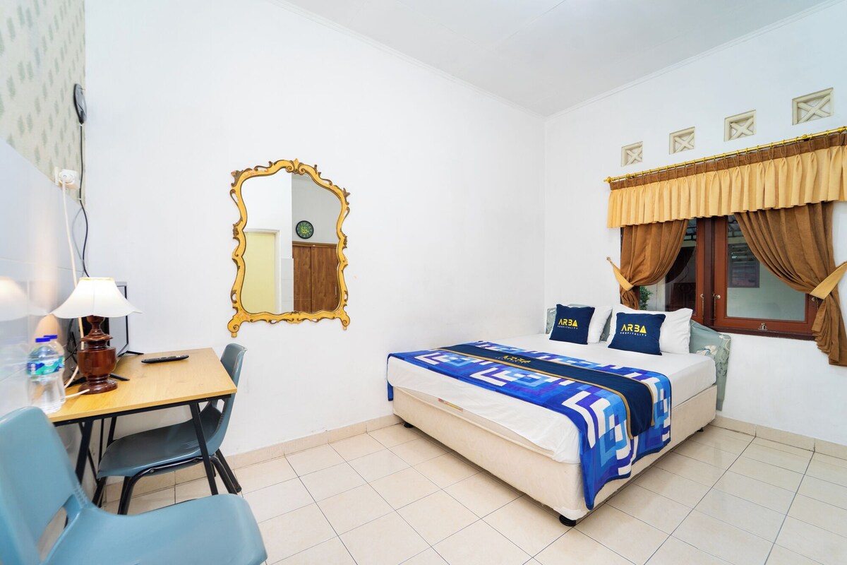 Hotellihuone, jossa on sänky, työpöytä, tuoli, peili ja ikkuna, jossa on verhot.