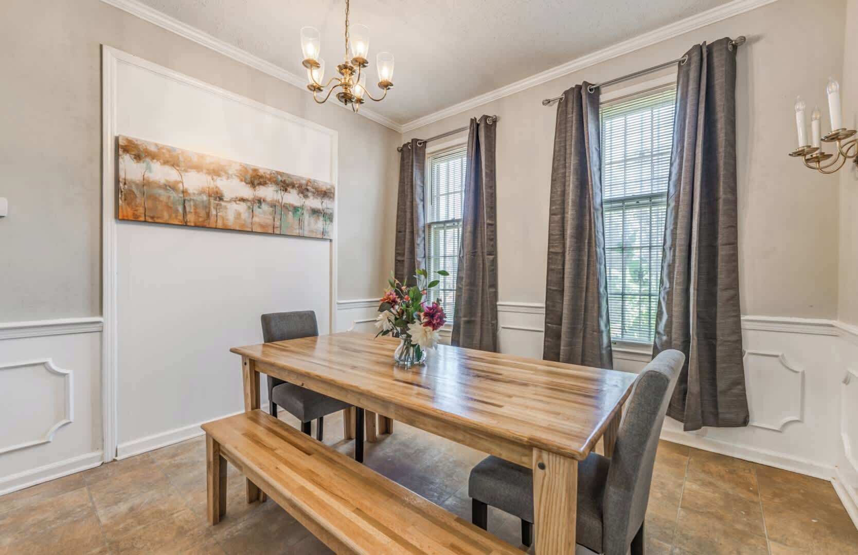 A dining room with a wooden table, chairs, a bench, a chandelier, and a painting on the wall.