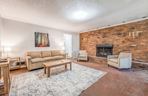 Ein Wohnzimmer mit Backsteinwand, Kamin, Sofa, zwei Sesseln, Couchtisch und Teppich.