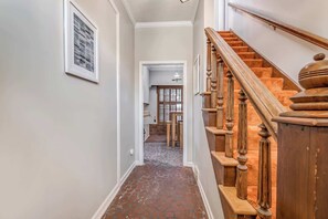 A hallway with a wooden staircase, a patterned floor, and a door leading to a dining area. - Near the Airport and Graceland! Holmesdale Hideout (Memphis)