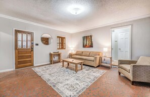 Ein Wohnzimmer mit einer Couch, einem Couchtisch, einem gemusterten Teppich, Holznachttischen, einem Spiegel und einem Gemälde an der Wand.
