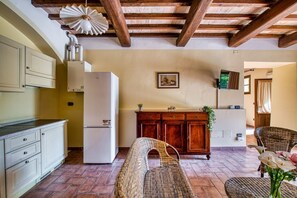 Eine Küche mit Kühlschrank, Holdekor, einem Korbstuhl und einem Essbereich mit Tisch und Stühlen.