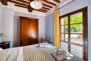 Ein Schlafzimmer mit Bett, Holzschrank, Stuhl, Lampe und einem Fenster mit Vorhängen.