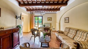 A spacious living area with a wooden ceiling, a sofa, wicker chairs, a dining table, and a cabinet. - GuestHost - Il Casale dei Gelsi - Tulipano (San Martino In Campo)