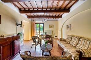 A spacious living area with a wooden ceiling, a sofa, wicker chairs, a dining table, and a cabinet. - GuestHost - Il Casale dei Gelsi - Tulipano (San Martino In Campo)