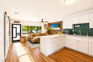 A modern kitchen with white cabinets, a central island, and a dining area with a sofa. - Private Oasis Near Beach - Heated Pool, Lounge, Bikes (Pompano Beach)