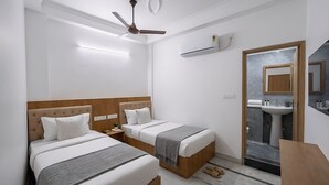 A hotel room with two beds, a ceiling fan, an air conditioning unit, a bathroom with a sink and mirror, and a marble-tiled floor. - Hotel Star City (New Delhi)