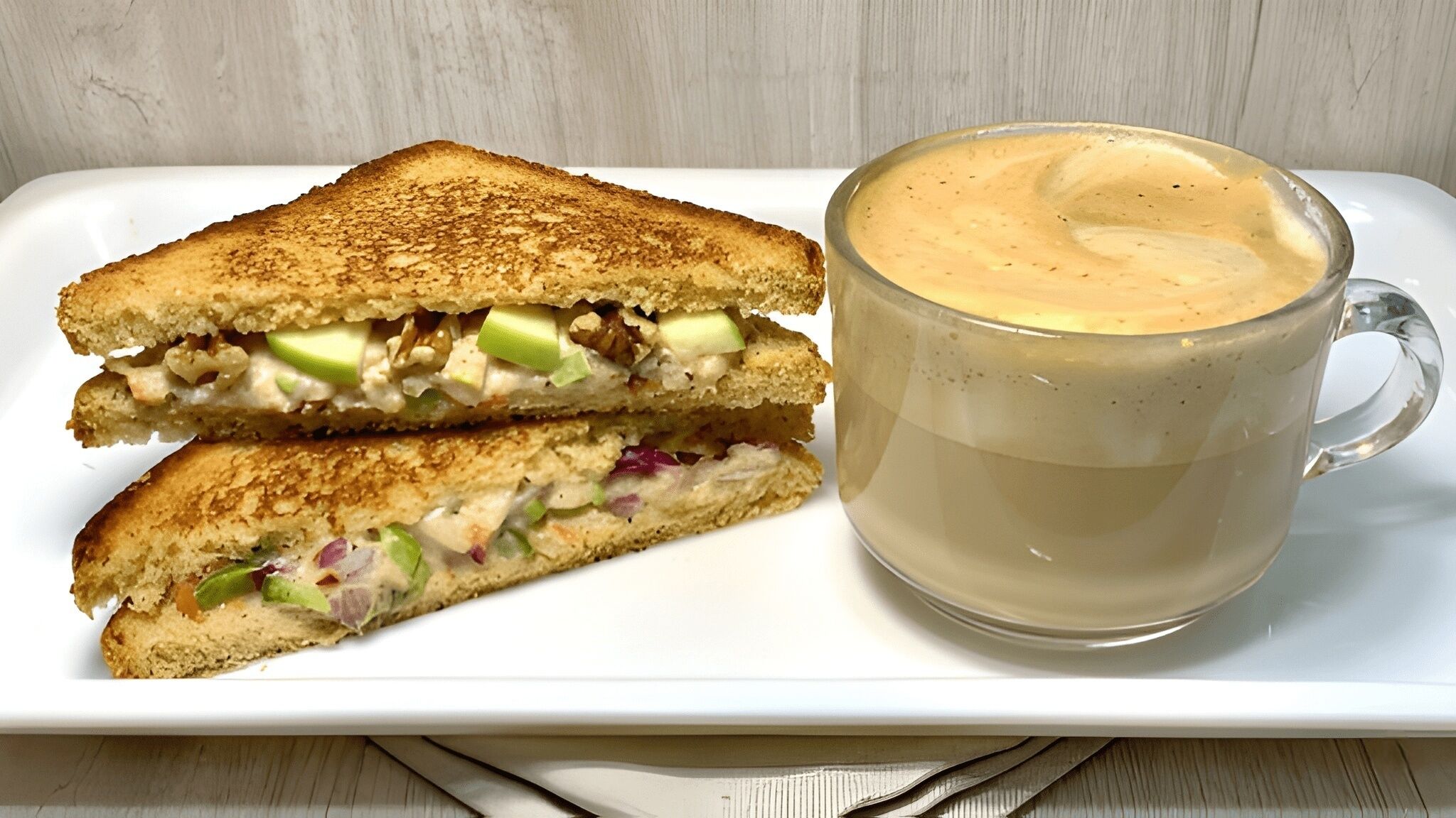 A sandwich cut in half and a cup of coffee on a white plate.