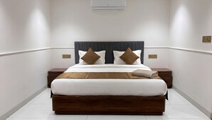 A modern hotel room with a large bed, a headboard, two bedside tables, and a wall-mounted air conditioner. - Hotel Star City (New Delhi)