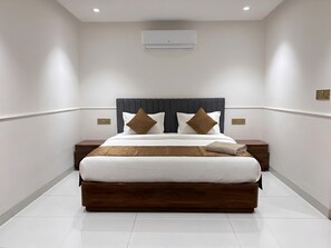 Una habitación de hotel moderna con una cama grande, un cabecero, dos mesitas de noche y un aire acondicionado instalado en la pared.