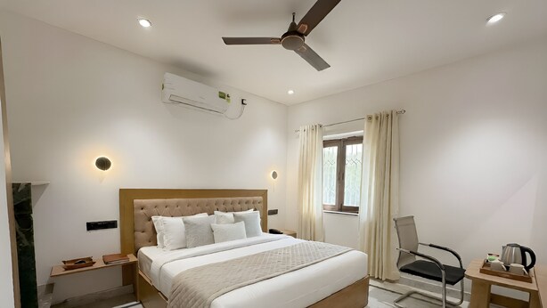 A hotel room with a bed, a desk, a chair, a ceiling fan, an air conditioning unit, and a window with curtains. - Hotel Star City (New Delhi)