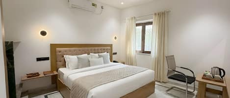 A hotel room with a bed, a desk, a chair, a ceiling fan, an air conditioning unit, and a window with curtains.
