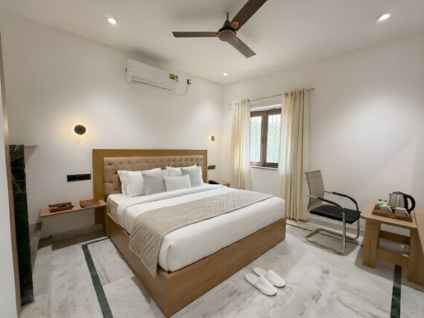 Habitación de hotel con cama, escritorio, silla, ventilador de techo, aire acondicionado y ventana con cortinas.