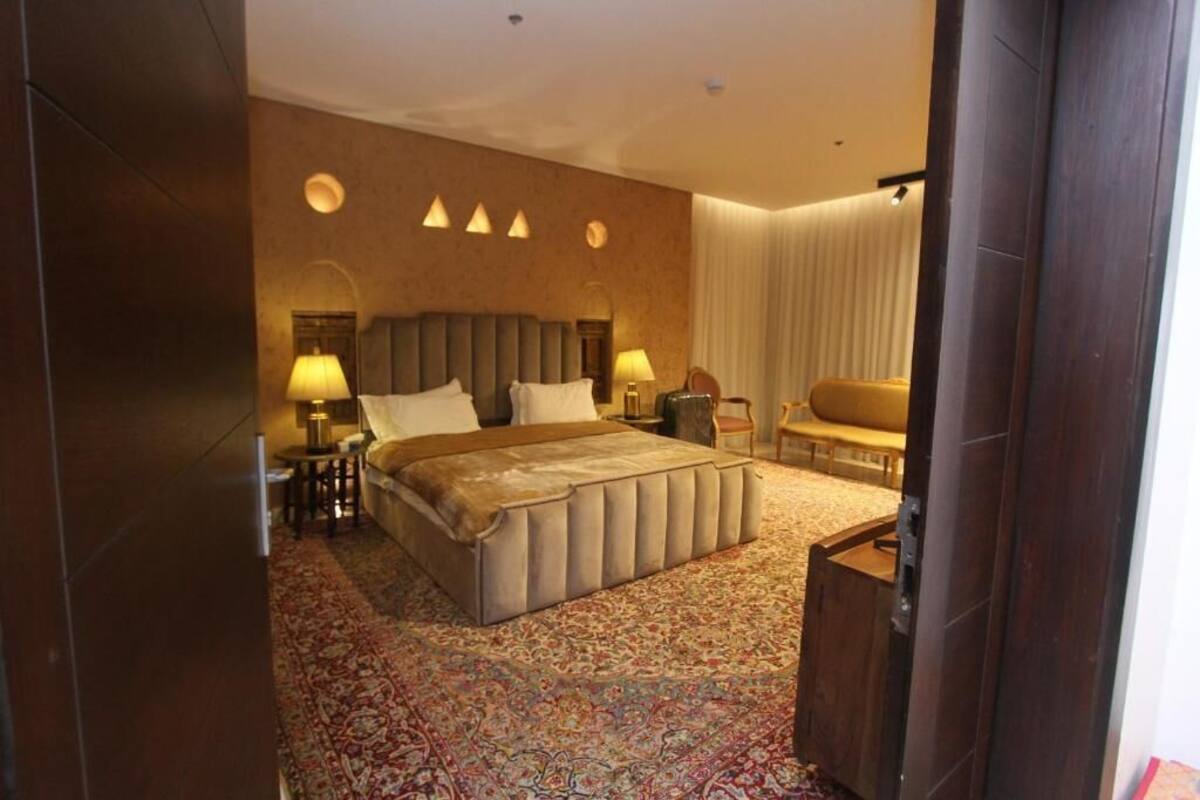 A hotel room with a large bed, two bedside tables with lamps, a sofa, and a patterned carpet.