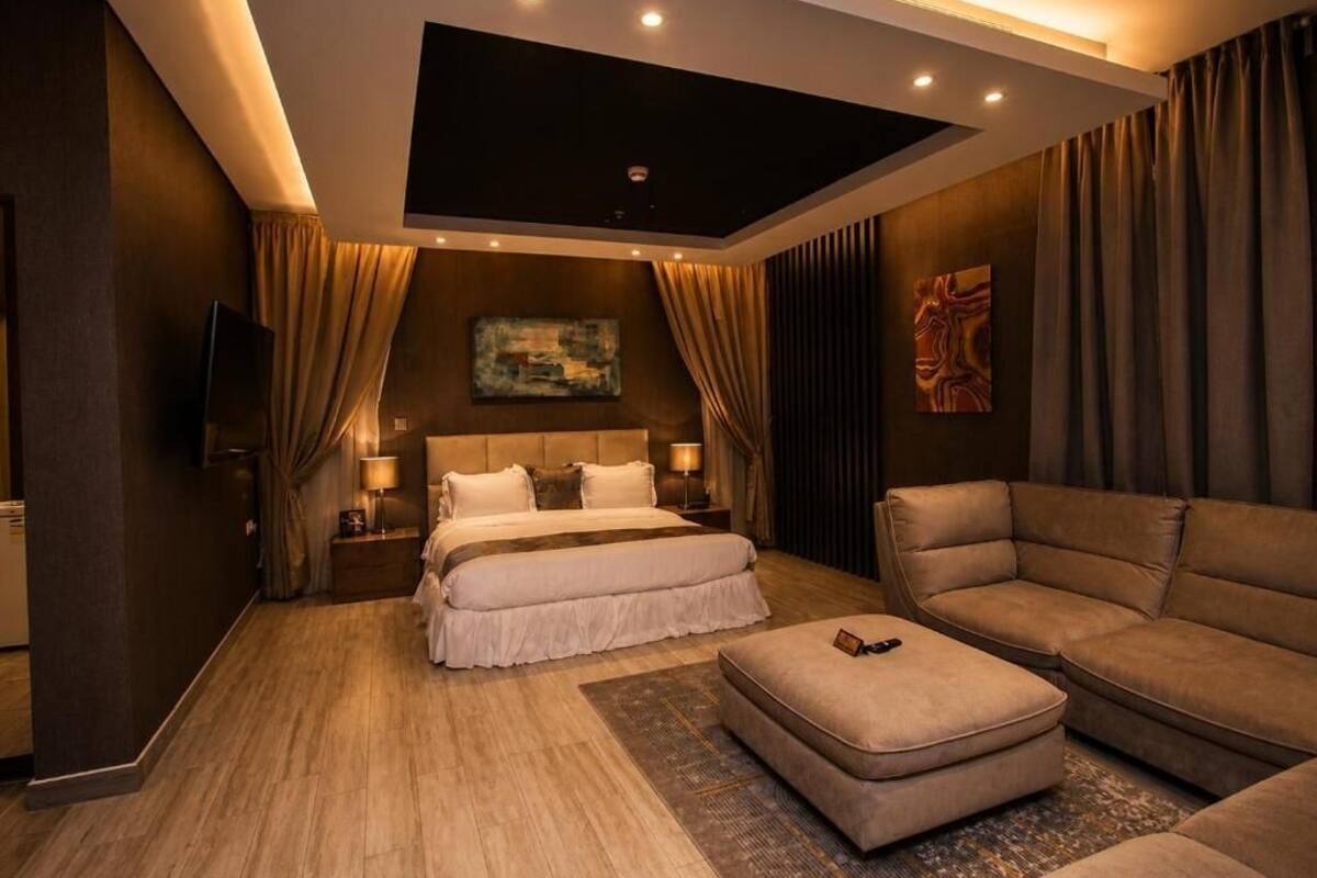 A modern hotel room with a bed, a sofa, a TV, and a painting on the wall.