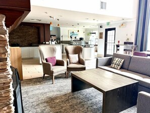 A modern hotel lobby with a seating area, a kitchen in the background, and a stone accent wall.