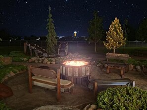 A night-time outdoor seating area with a fire pit, benches, and a view of the sky.