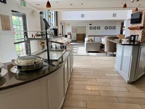 A hotel lobby with a buffet area, a seating area, and a kitchen counter. - Suite with Full Kitchen | Free Breakfast & Pool (Great Falls)