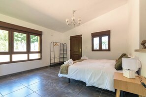 Un dormitorio con cama, mesita de noche de madera, lámpara, perchero y una puerta.