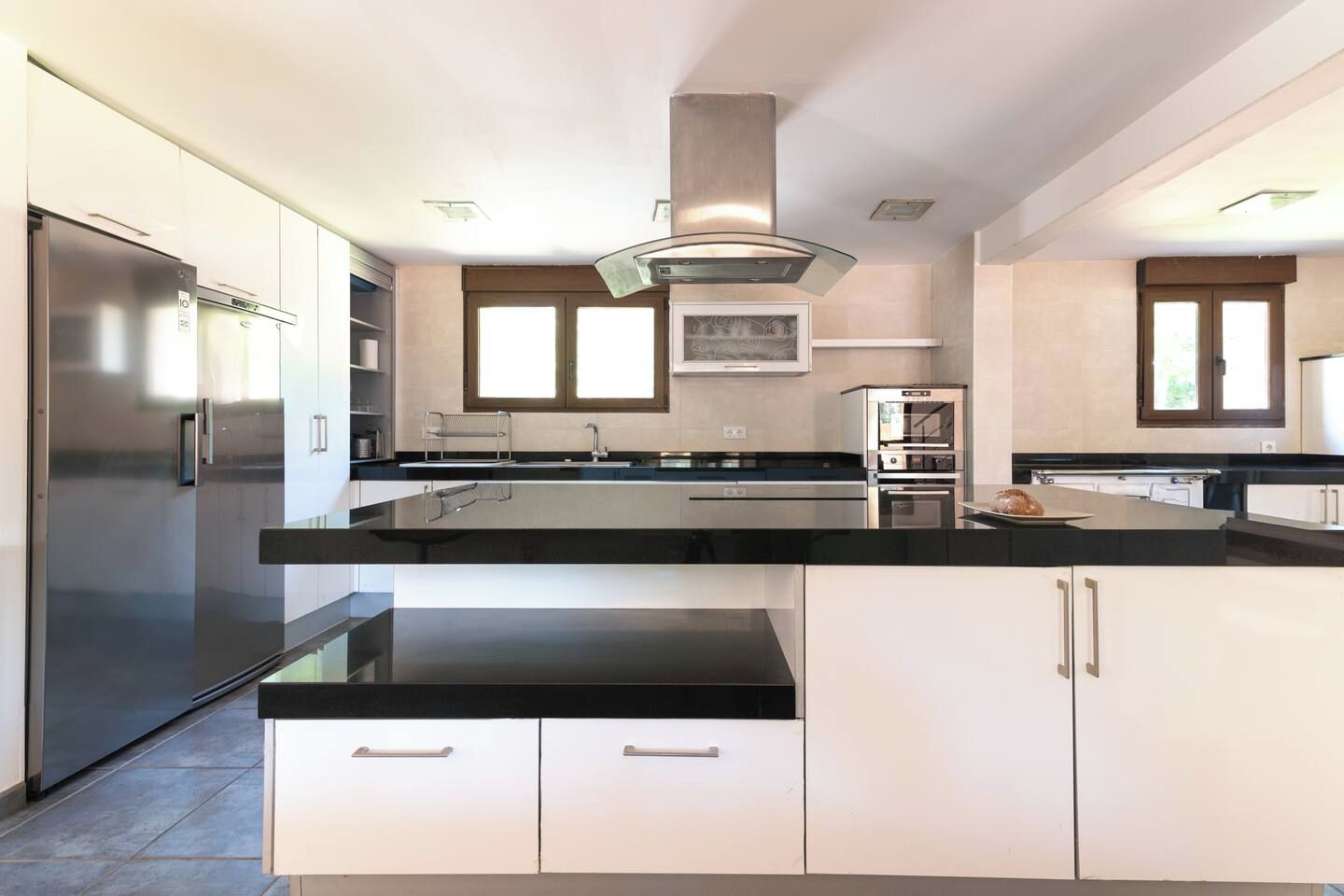 Una cocina moderna con un refrigerador de acero inoxidable, dos hornos y una encimera negra.