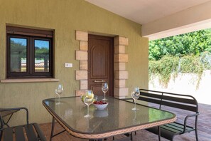 An outdoor patio with a glass table, two chairs, and a bowl of fruit.