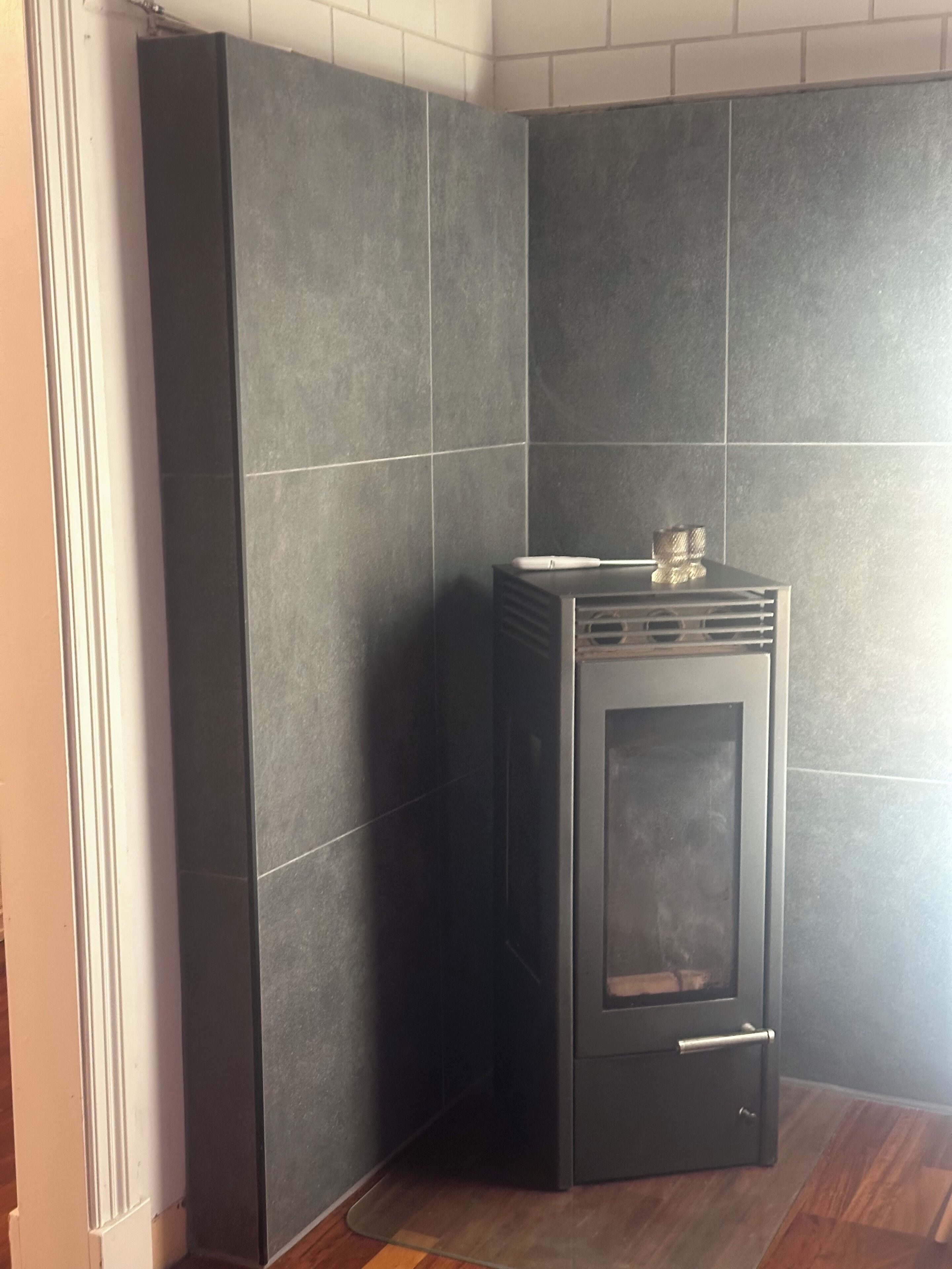 A corner room with dark grey tiled walls, a built-in wood stove, and a wooden floor.