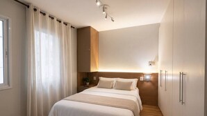 Une chambre à coucher comprenant un lit, des rideaux, une table de chevet, une lampe fixée au mur et une armoire.